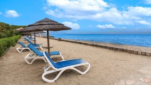 A beach with sun loungers and thatched umbrellas.