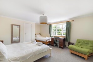 A bedroom with two beds, a desk, a chair, a green sofa, a hanging light fixture, and a window with curtains.