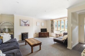 A living room with a fireplace, sofa, coffee table, TV, and a window with curtains.