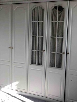 Ein weißer Kleiderschrank mit mehreren Türen und einem mittigen Fenster mit Vorhängen.