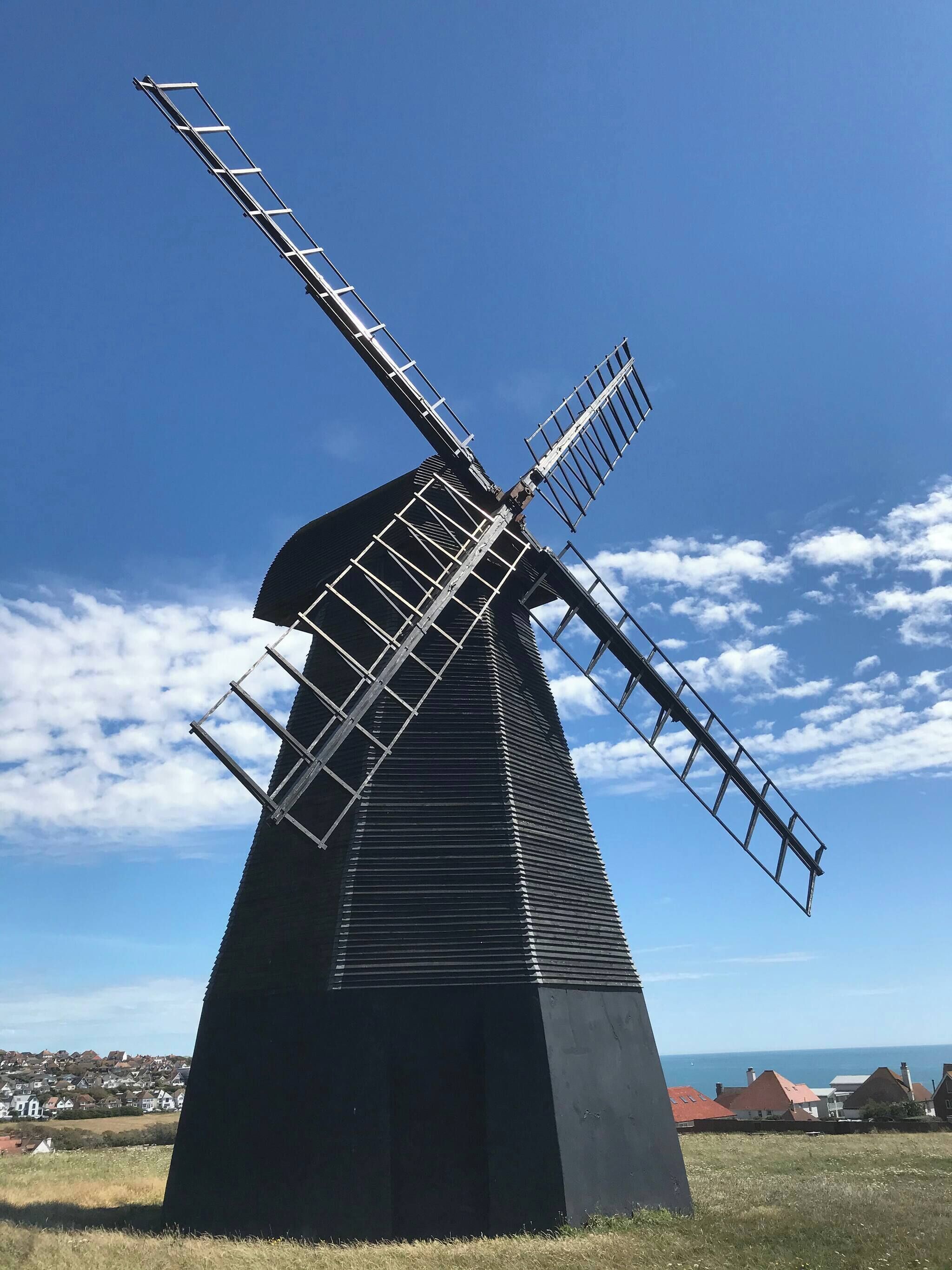 Un molino de viento con una viga metálica y una base negra, frente a un cielo despejado con nubes.
