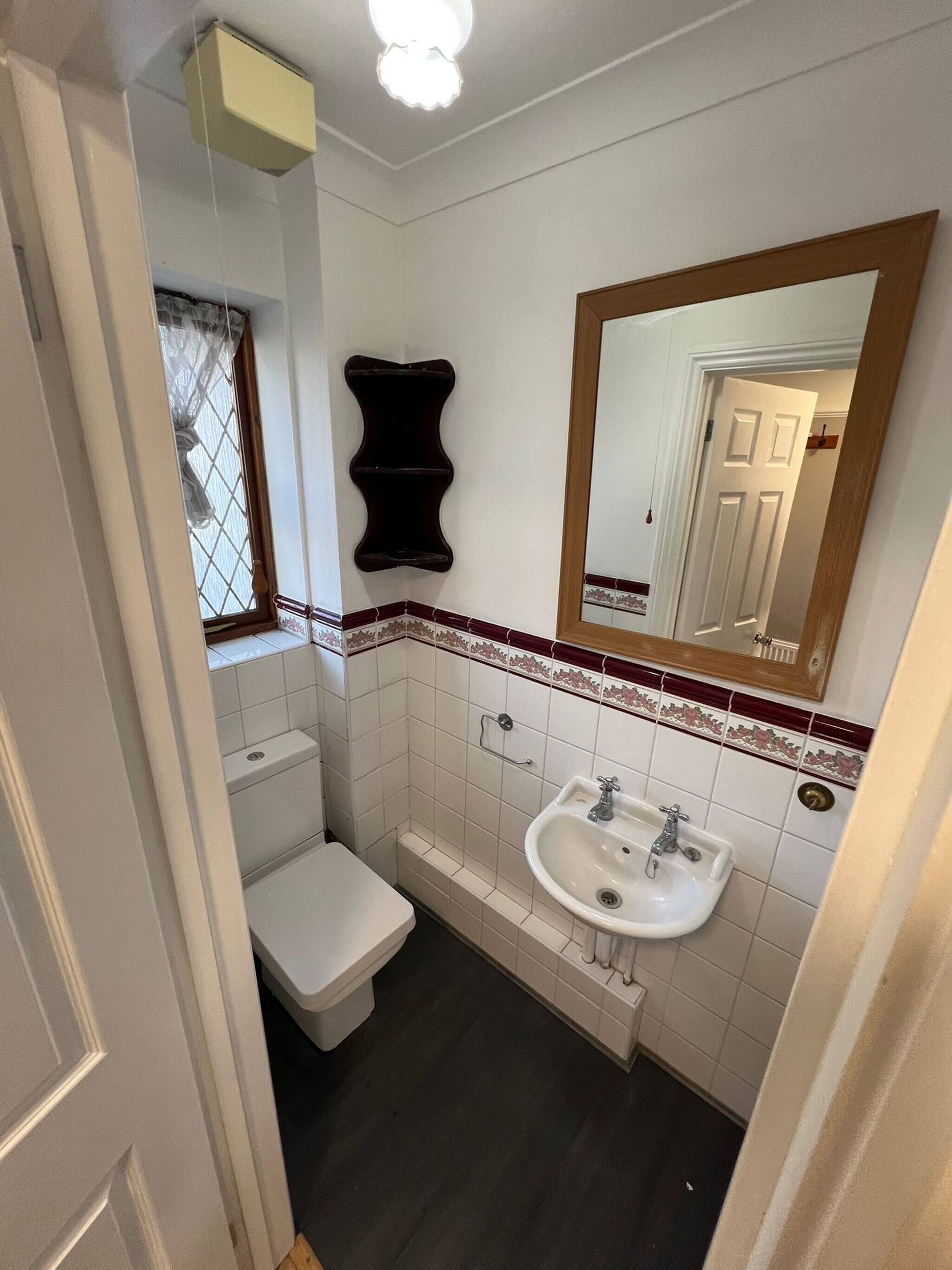 A bathroom with a toilet, sink, mirror, and decorative wall tiles.
