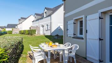 Une terrasse avec une table dressée pour le petit-déjeuner, des chaises blanches et une porte blanche.