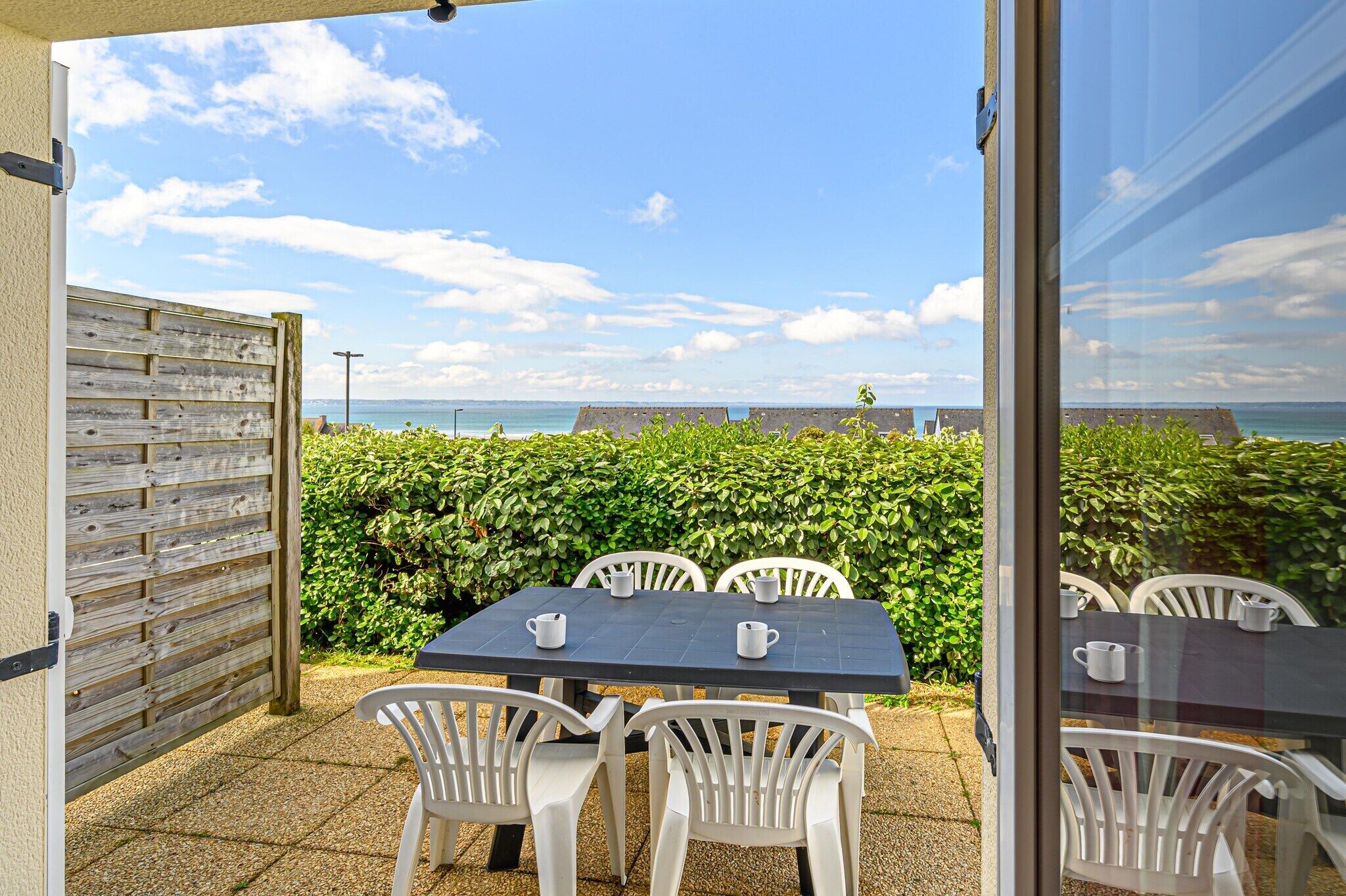 Une terrasse extérieure avec une table et des chaises, une clôture en bois et une vue sur la mer.