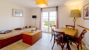 A room with a bed, a table, chairs, a TV, and a balcony with a view. - Brittany Flat near Pentrez Beach (St Nic)