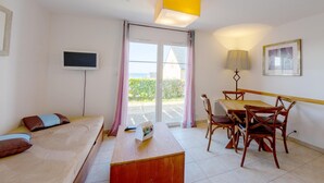 A hotel room with a bed, a desk, a dining table with chairs, a television, a lamp, and a sliding glass door leading to an outdoor area. - Brittany Flat near Pentrez Beach (St Nic)