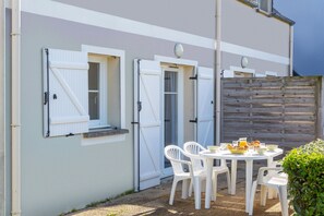 A patio with a table and chairs, a wooden fence, and a building with white doors and windows. - Brittany Flat near Pentrez Beach (St Nic)