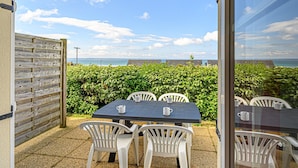 Une terrasse extérieure avec une table et des chaises, une clôture en bois et une vue sur la mer.