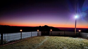 A nighttime scene with a white picket fence, a grassy area, and a distant mountain range under a twilight sky. - Himaaksh Uttarakhand  (Sigri)