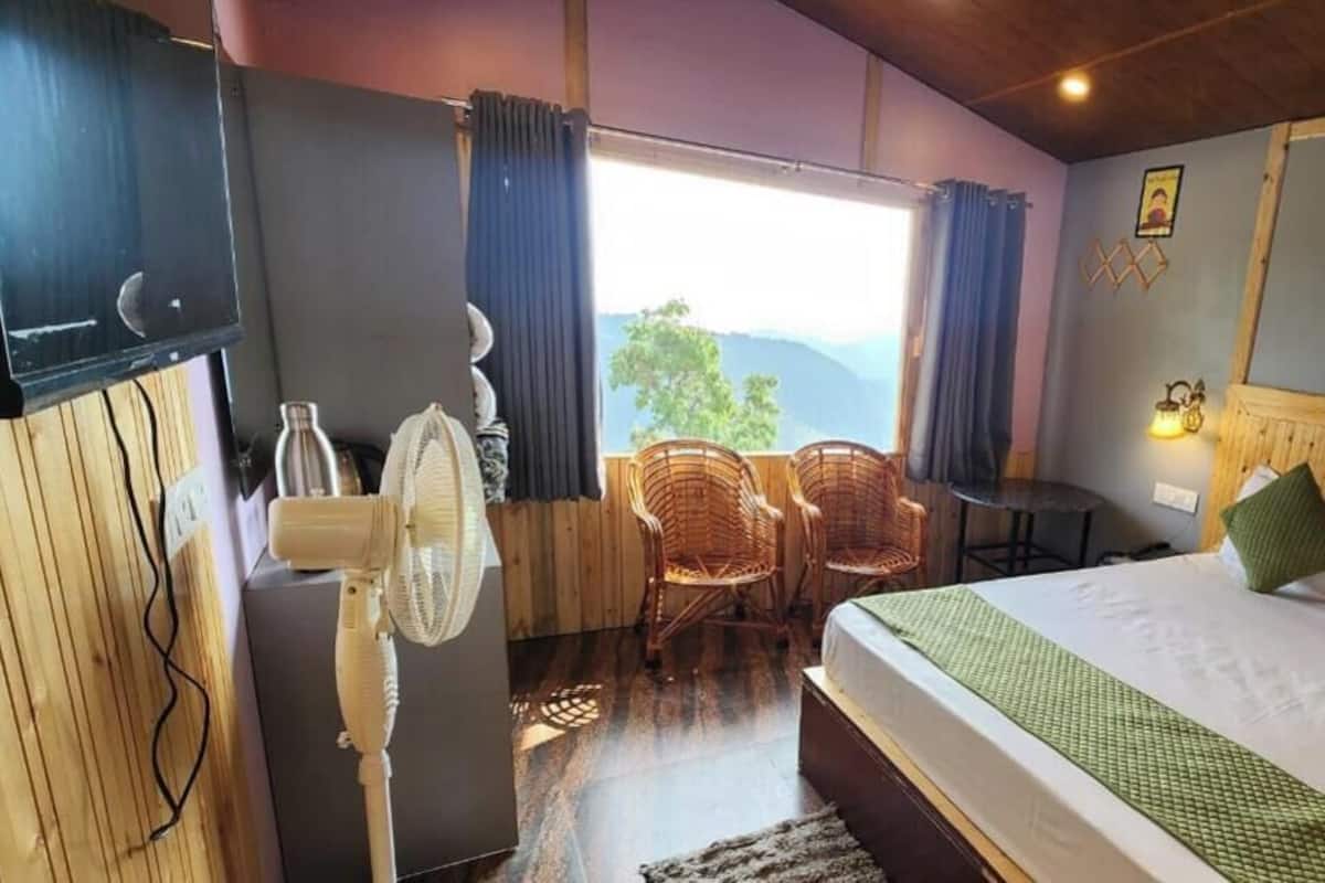 A bedroom with a bed, two wicker chairs, a small table, a fan, and a view of the outdoors.