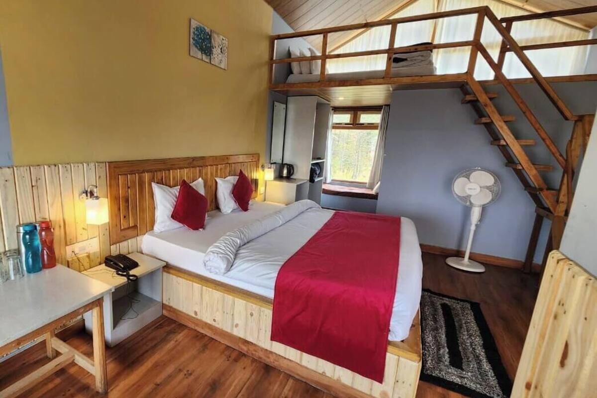 A bedroom with a bunk bed, wooden headboard, bedside table, lamp, and a fan.