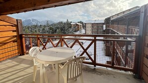 Un balcón de madera con una mesa y sillas, que da a un paisaje nevado de montañas y edificios.