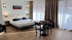 Habitación de hotel con cama, mesitas de noche, una mesa de comedor con sillas y un ventanal con cortinas.