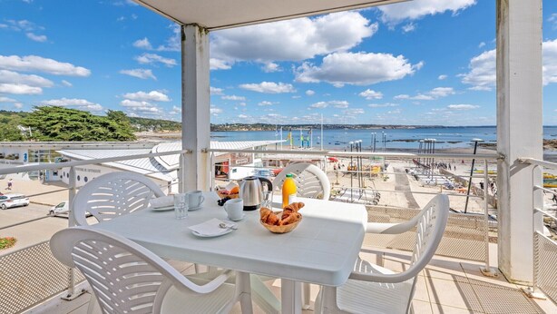 A balcony with a table set for breakfast, overlooking a beach and cityscape. - Stay with Indoor Pool & Sea (Plougonvelin)