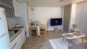 Ett kompakt kök med mikrovågsugn, diskho och tvättmaskin, en matplats med bord och stolar, en platt-TV och en liten sittgrupp med soffa och soffbord.