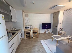 Eine kompakte Küche mit Mikrowelle, Spüle und Waschmaschine, ein Essbereich mit Tisch und Stühlen, ein Flachbildfernseher und eine kleine Sitzecke mit Sofa und Couchtisch.