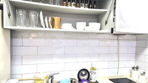 Ett kök med en diskho, ett diskställ, en hylla med glas och flaskor samt en mikrovågsugn.