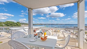 A balcony with a table set for breakfast, overlooking a beach and cityscape.