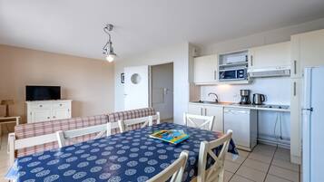 A compact room with a dining table, chairs, a television, a kitchenette, and a bathroom door.