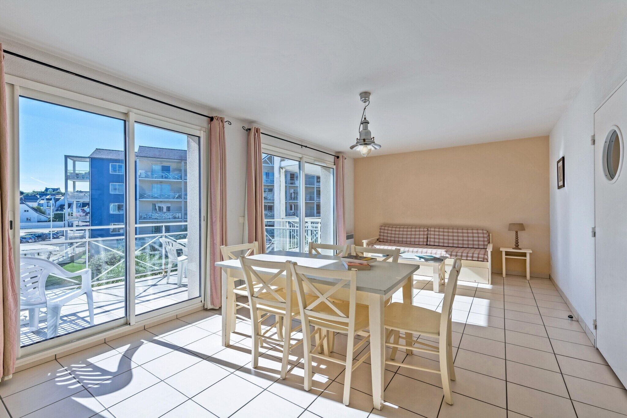 A balcony with a view of buildings, a dining table with chairs, a sofa, and a lamp.