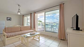Una sala de estar con sofá, mesa de centro, televisor y ventanas grandes con cortinas.
