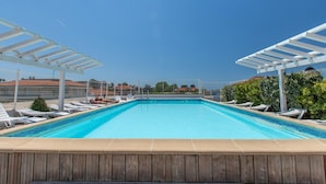 A rectangular swimming pool with a wooden deck in the foreground, surrounded by white lounge chairs and a pergola structure. - Coastal Stay for 4 in Cagnes-sur-Mer (Cagnes-sur-Mer)