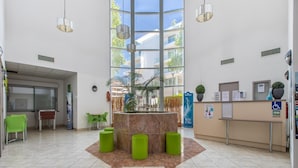 A lobby with a reception desk, green chairs, a central plant, and a large window. - Coastal Stay for 4 in Cagnes-sur-Mer (Cagnes-sur-Mer)