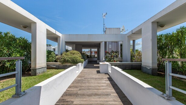 A modern building with a central open space, white pillars, and a wooden walkway leading to a covered entrance. - Coastal Stay for 4 in Cagnes-sur-Mer (Cagnes-sur-Mer)