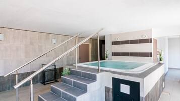 A modern indoor pool area with a staircase leading to a spa, surrounded by neutral-toned walls and a minimalist design.