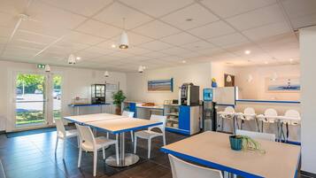 A modern restaurant with white and blue decor, a kitchen area, and a view of the outdoors.