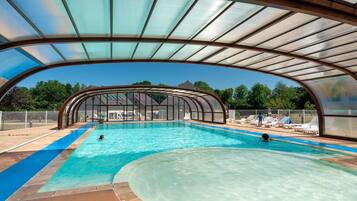 A covered swimming pool with a curved roof, clear blue water, and lounge chairs around the perimeter.