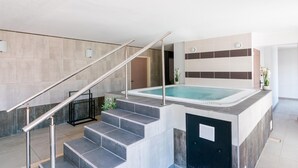 Un área de piscina interior moderna con una escalera que conduce a un spa, rodeada de paredes en tonos neutros y un diseño minimalista.