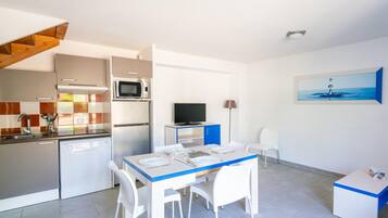 Una cocina compacta con electrodomésticos modernos, un comedor con sillas blancas y un televisor.