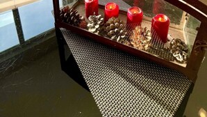 Una stanza con un tavolo in vetro su cui sono disposti pigne e candele rosse, un camino a legna e un televisore fissato alla parete.