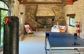 Ein Zimmer mit einer Tischtennisplatte, einer Hängematte, einem Boxsack und einer Steinwand.