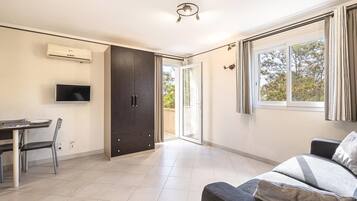 Uma sala de estar moderna com sofá, televisão, área de jantar com mesa e cadeiras, e porta de vidro deslizante que dá para uma área externa.