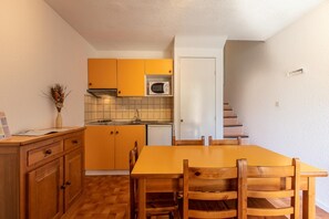 A compact kitchen with wooden cabinets, a microwave, and a dining table with chairs. - Spacious apartment for 5-persons (GUILLAUMES)