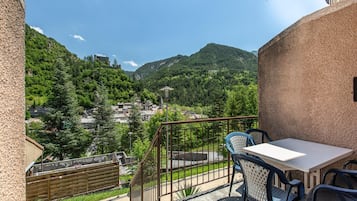Un balcon avec une table et des chaises, donnant sur un paysage montagneux parsemé de bâtiments.