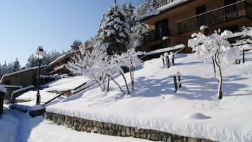 A snow-covered building with a stone wall, a balcony, and snow-laden trees.