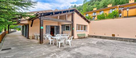 Un edificio con un patio cubierto, mobiliario exterior y vistas a una ladera.