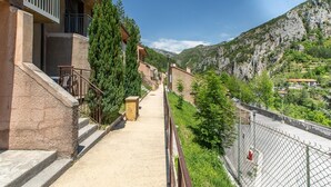Um edifício residencial com escadaria que leva a uma varanda, rodeado por vegetação e montanhas ao fundo.
