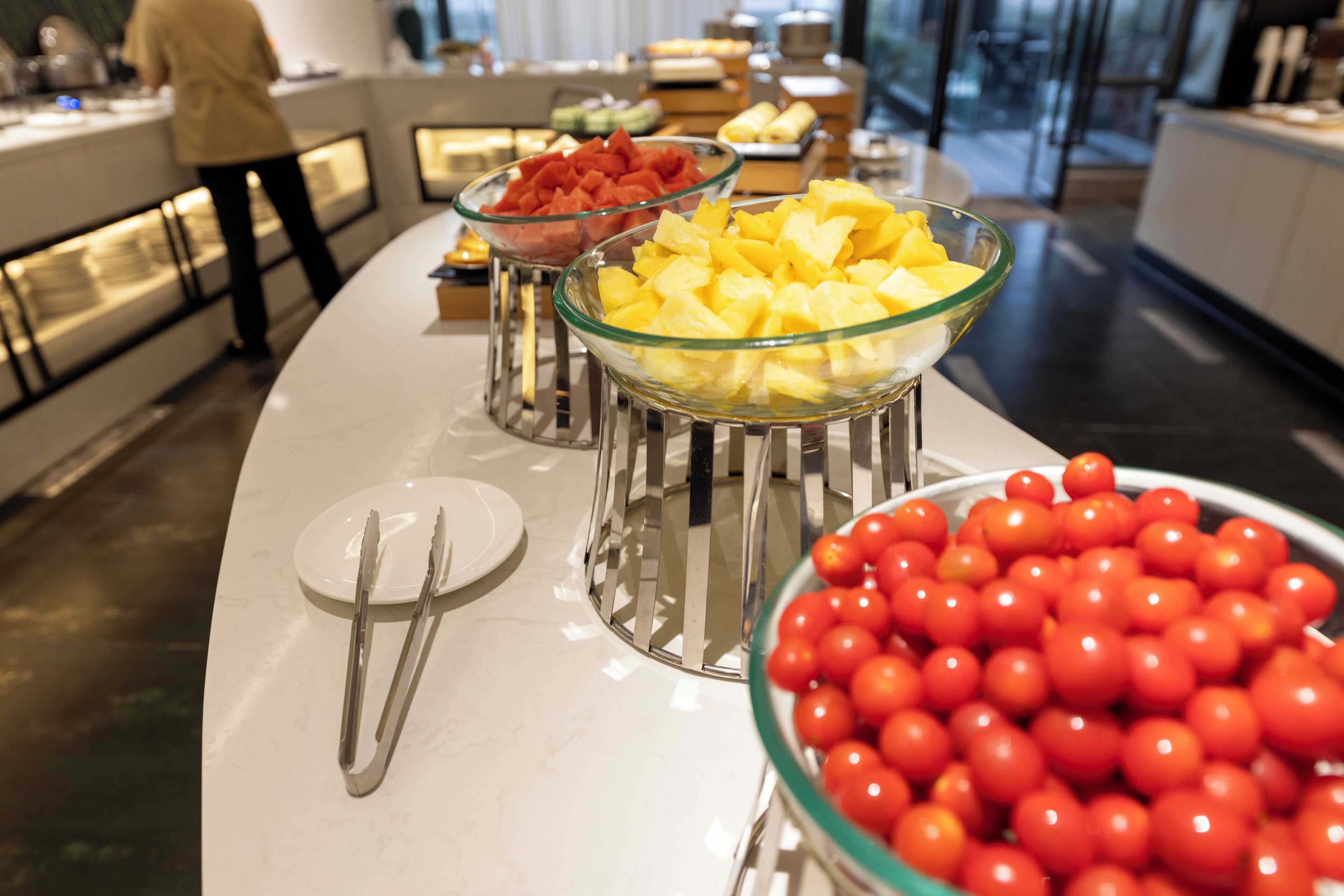 A buffet with bowls of fruit and a plate with cutlery.