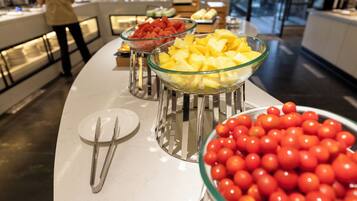 A buffet with bowls of fruit and a plate with cutlery.