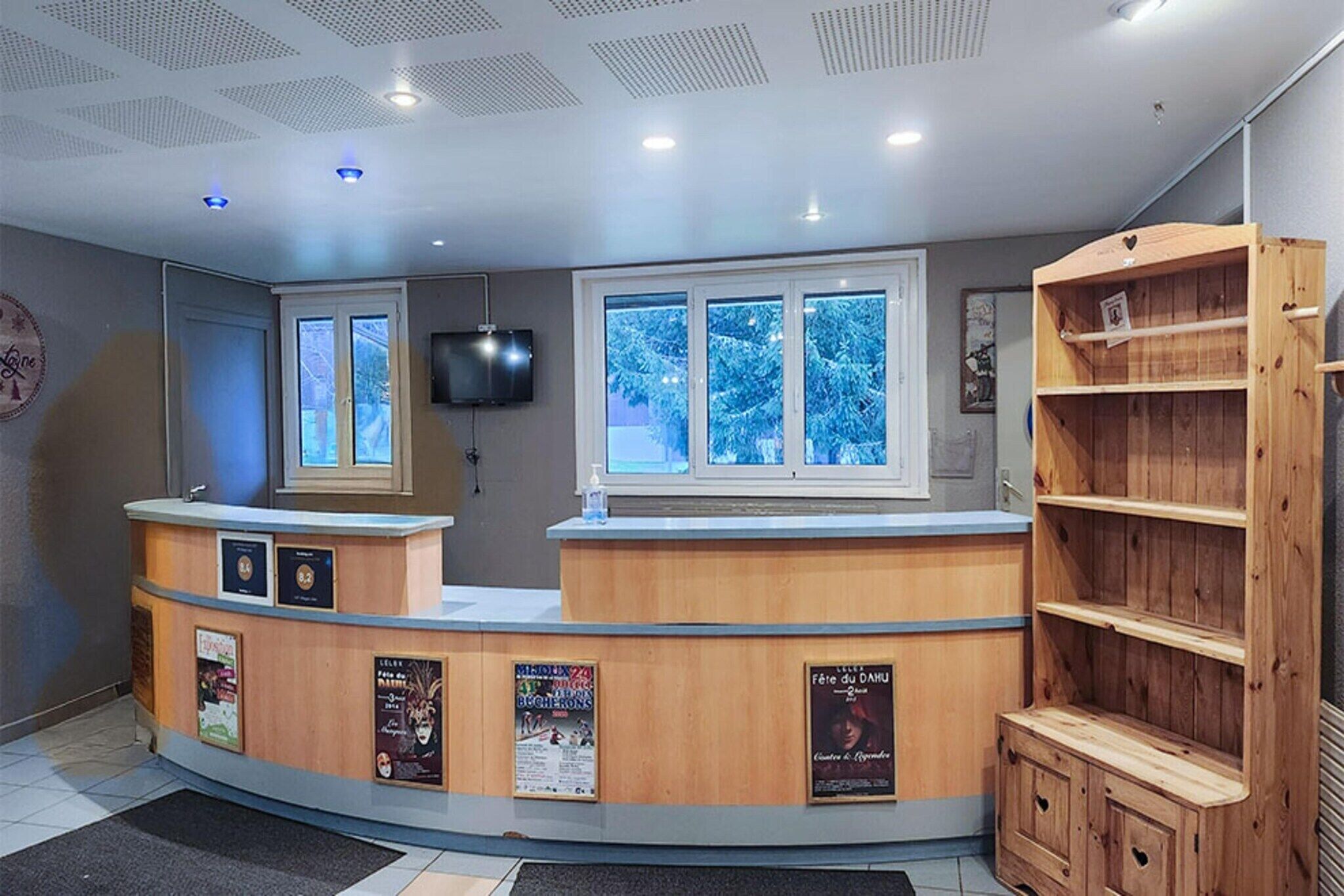 A reception desk with a TV, a window with a view of snow-covered trees, and a wooden bookshelf.