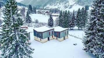 A snow-covered building with a curved roof, surrounded by snow-laden trees and a mountainous backdrop.
