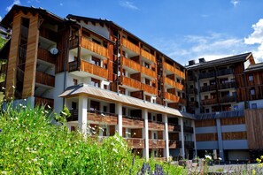 A multi-story hotel with balconies, a covered entrance, and a garden area. - Cozy 1-Bedroom Rental for 4 (ORCIERES  MERLETTE)