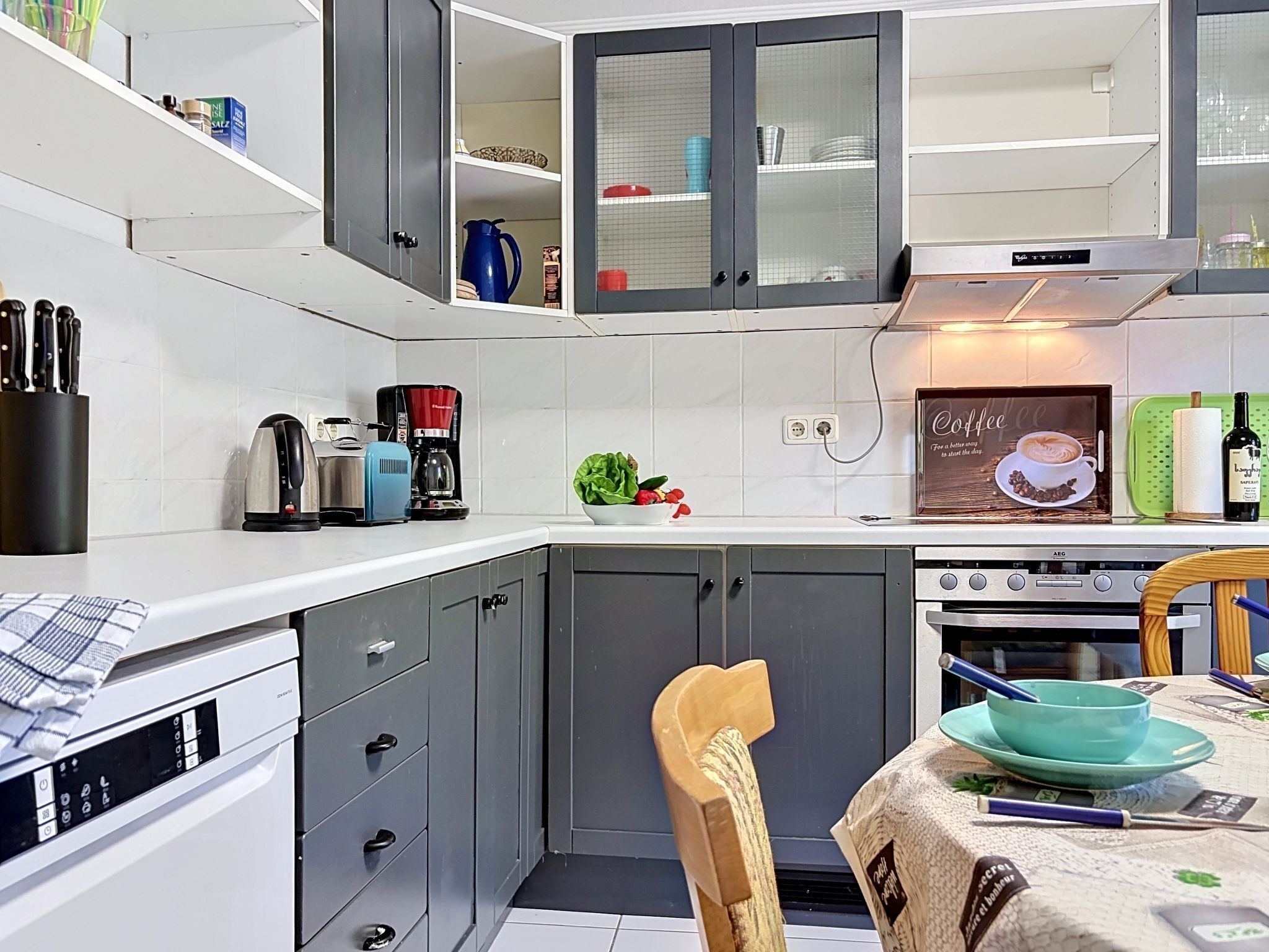 A compact kitchen with a coffee maker, a kettle, and a toaster. There is a dining area with a table and chairs.