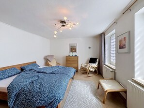Une chambre à coucher comprenant un lit, deux chaises, une commode, un miroir et une fenêtre avec des stores.