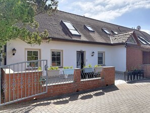 Une maison avec un toit en tuiles, un mur en briques et une entrée fermée par un portail.