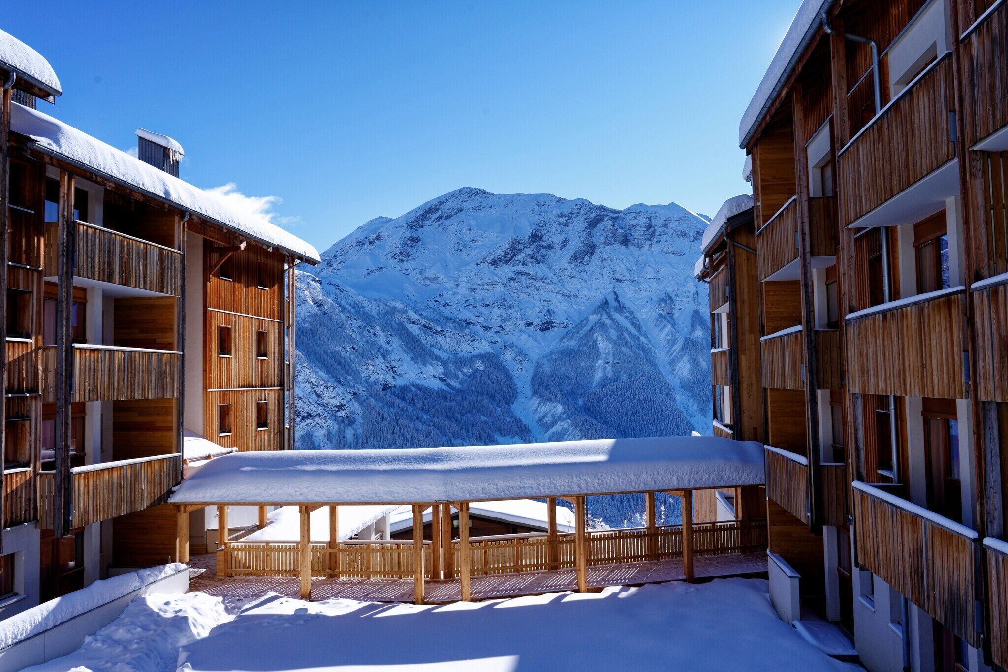 Un edificio de madera con balcones y una mesa cubierta de nieve en primer plano, con una montaña al fondo.